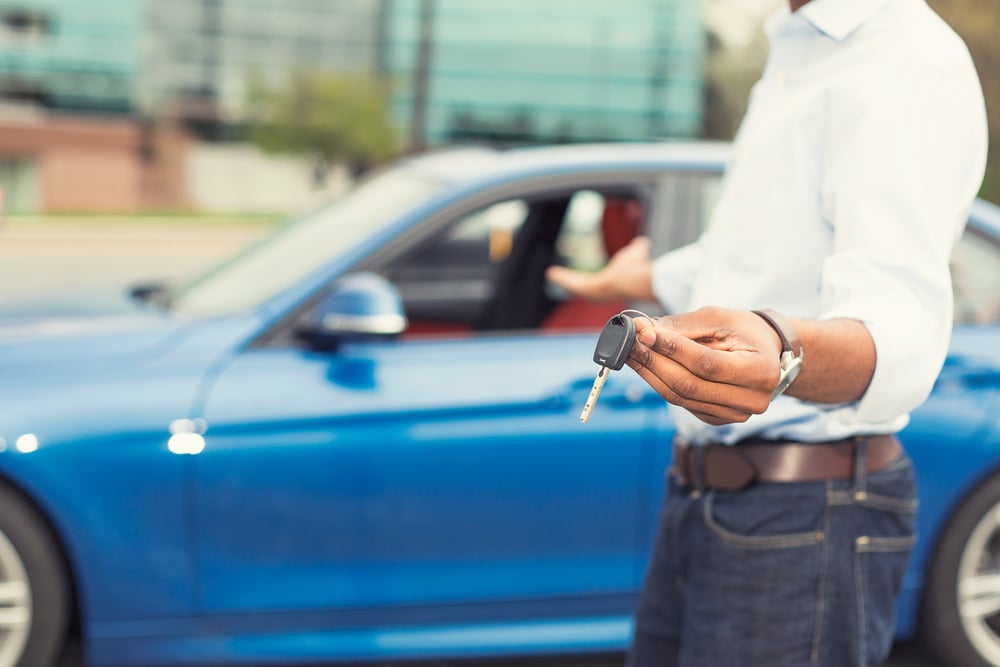 man holding keys in front of blue car